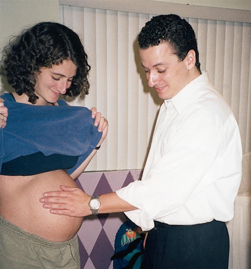 A man looking at the baby bump of a pregnant woman with his hand placed over it.