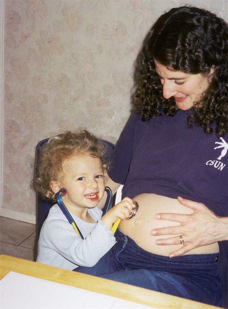 A child with a toy stethoscope feels the sound of her unborn sibling across her pregnant mother's belly.
