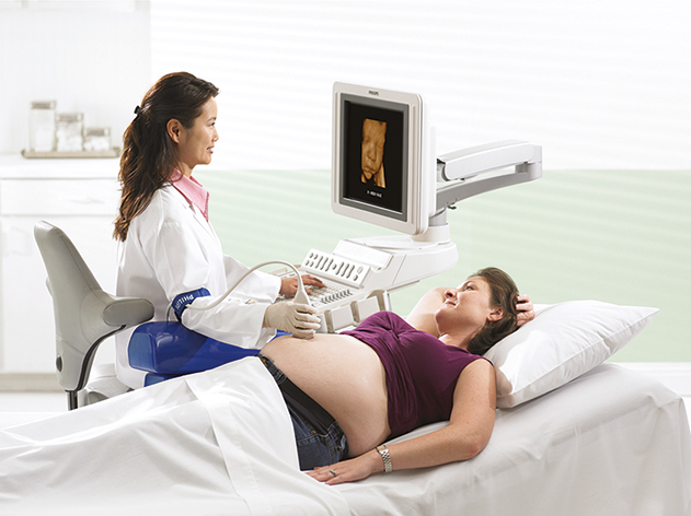 A sonographer is scanning the abdomen of a pregnant woman using a transducer probe while observing the images on a monitor.