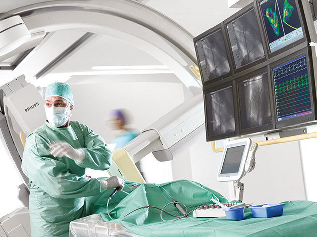 A physician performs a cardiovascular interventional procedure in a surgical suite with multiple monitors displaying various images.
