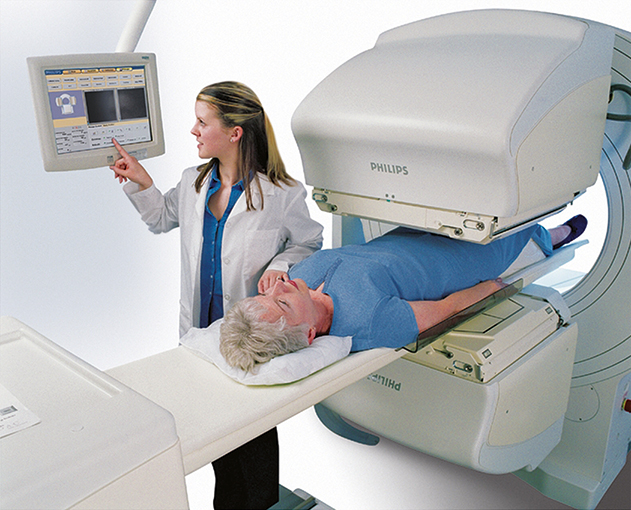 A patient is lying against her back on an invivo detection scintillation camera while a doctor is viewing the reading displayed on the monitors.
